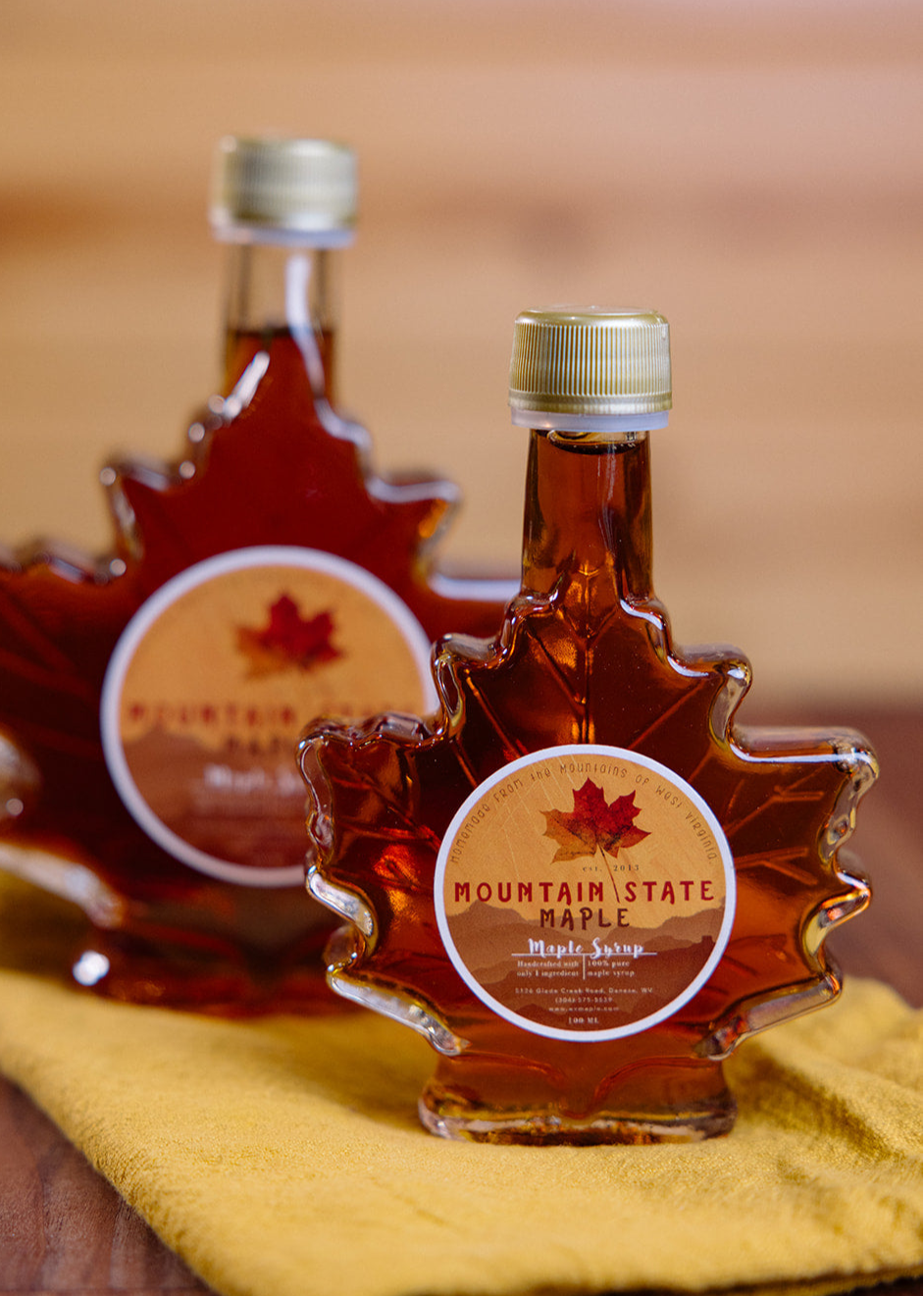 Two bottles of Mountain State Maple Syrup on a wooden surface with a blurred background